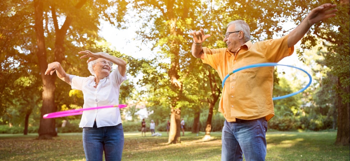 Happy funny senior couple playing hulahop in park-613759588