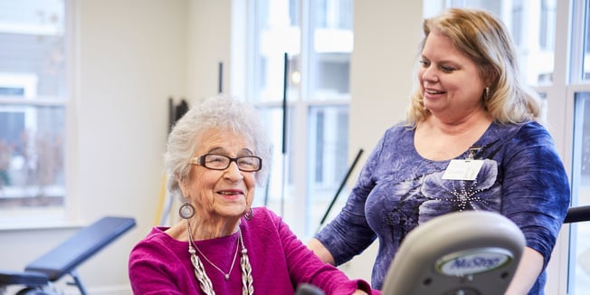 Senior living employee helping senior woman exercise