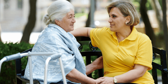 A senior woman and her daughter sit on a bench