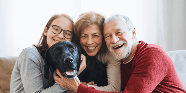 An adult child with senior parents and a pet dog hugging each other and smiling