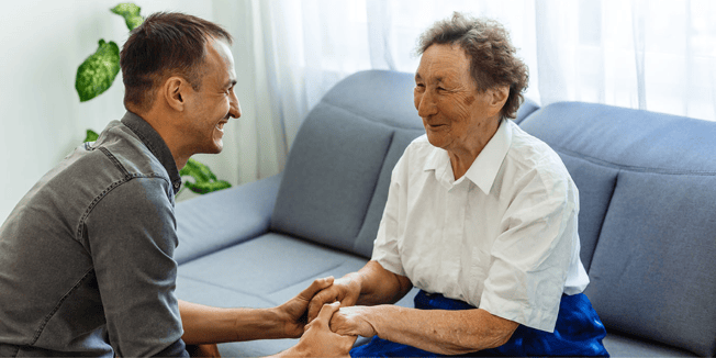 A caregiver comforts a dementia care resident by holding her hands and smiling