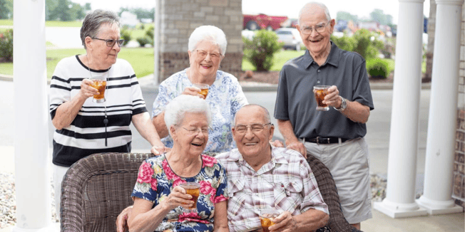 Senior residents of a community toasting drinks together while sitting outside