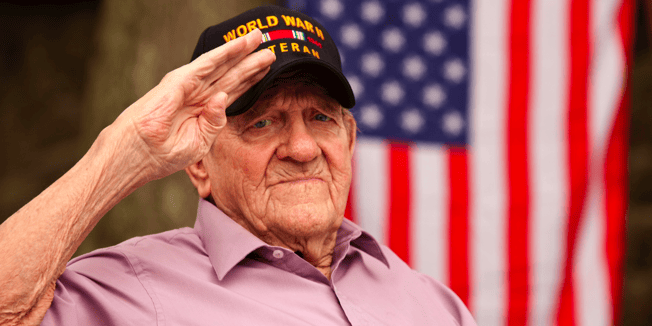 A senior wearing a World War 2 Veteran hat and saluting