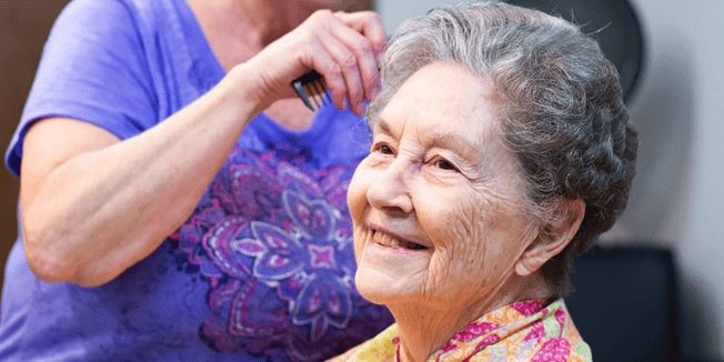 An assisted living caregiver brushes the hair of a senior living resident