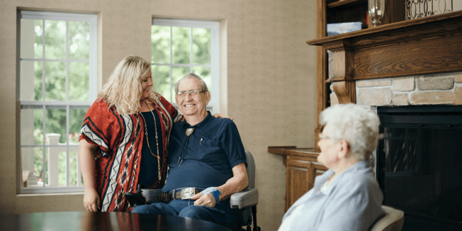  A senior caregiver stands next to an elderly man in a motorized wheelchair as they discuss transitioning from a hospital to an assisted living community