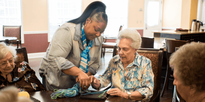 An employee in a senior living community helps a resident with a craft project