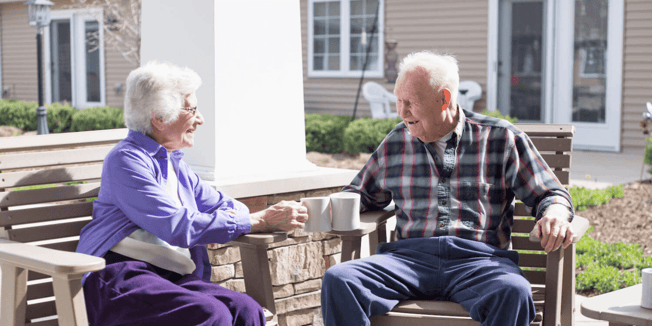 Two senior living residents enjoying coffee together while sitting outside