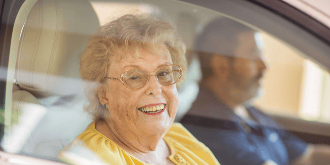 smiling senior seated in car passenger seat with family member driving