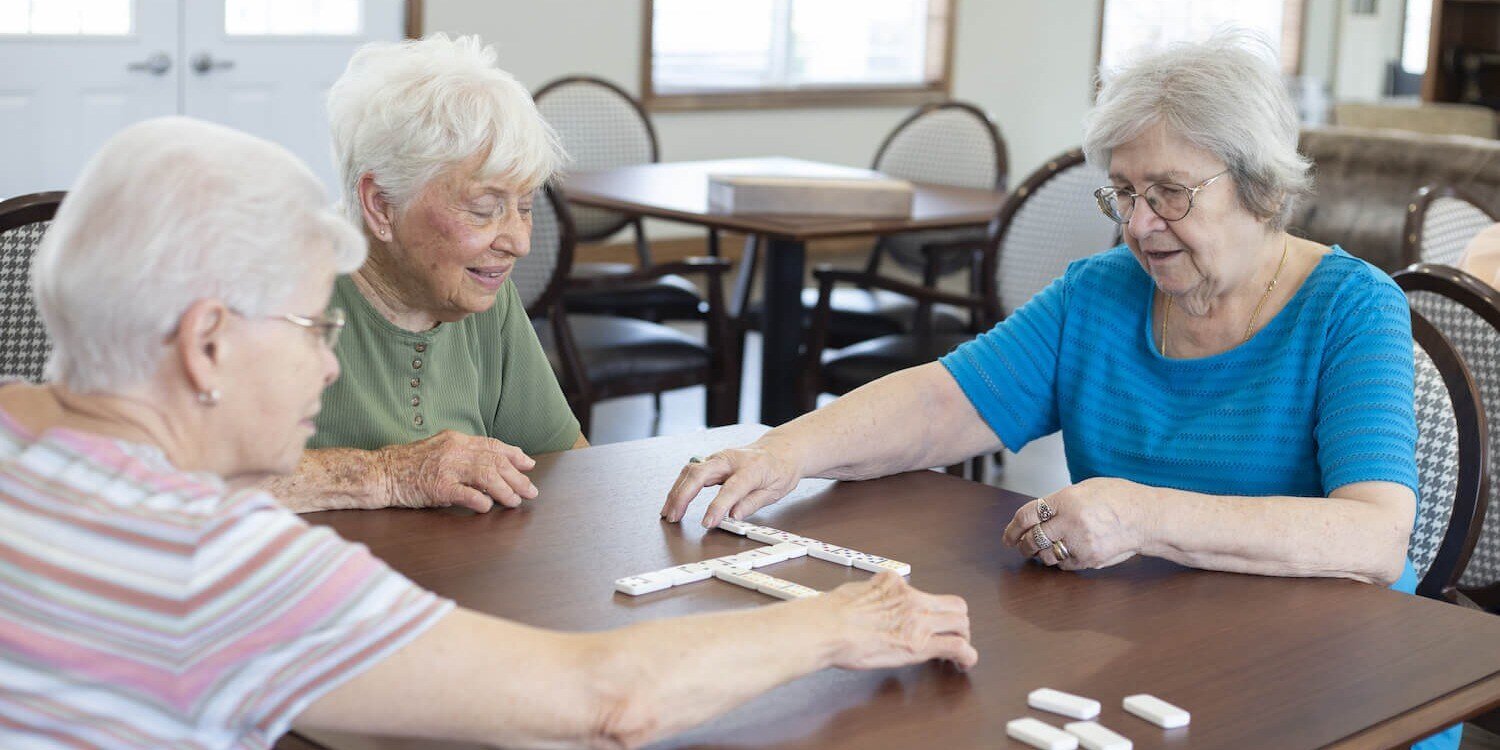 Group of senior residents around table playing a game of dominos in a memory care community
