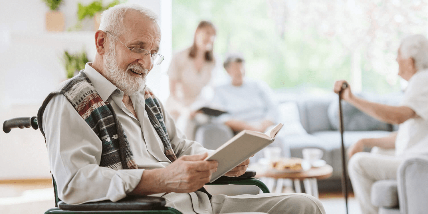 Senior living resident with glasses reading in his wheelchair